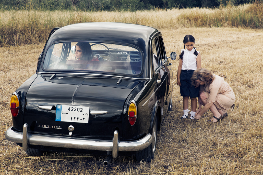 ﻿Woman fixing girl's sock in field with old car parked next to them