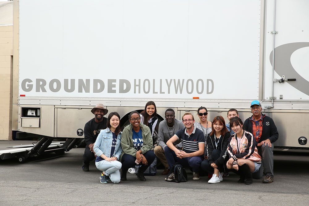 NYFA acting class posing for a group photo in front of a Grounded Hollywood trailer.