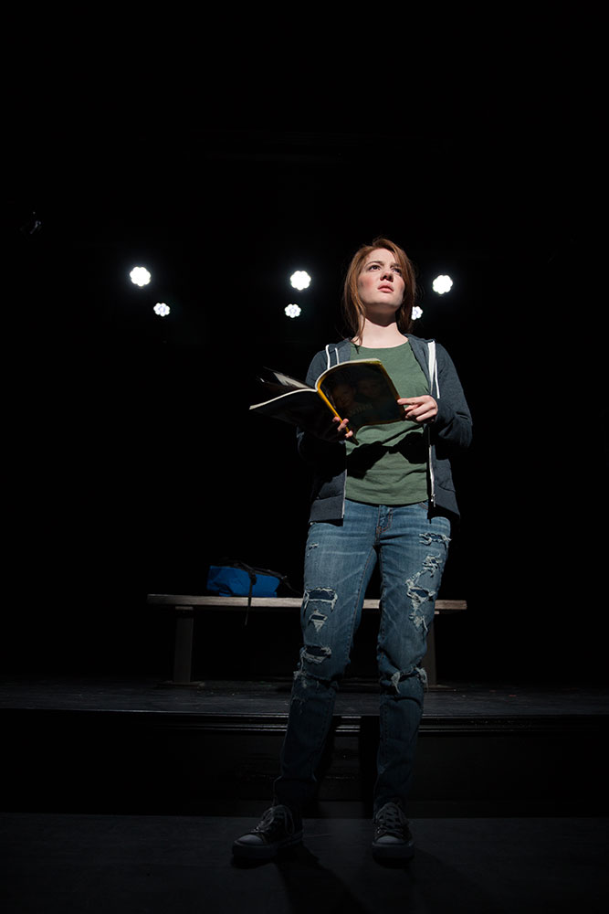 NYFA And Then They Fell actress performing alone center stage with a book under spotlight.