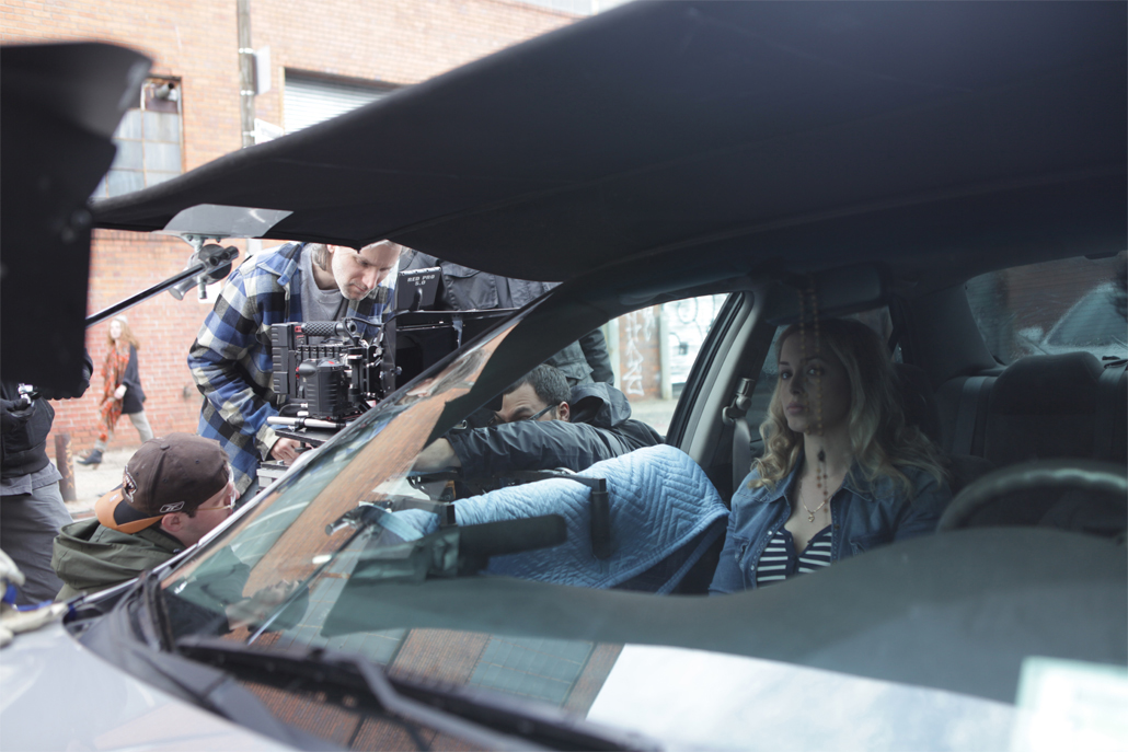 Crew members adjusting car camera rig while actress waits in the car