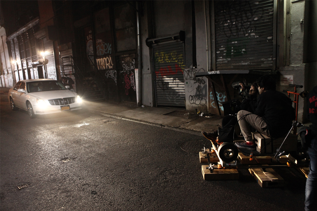 Two men in an alley filming a white car at night