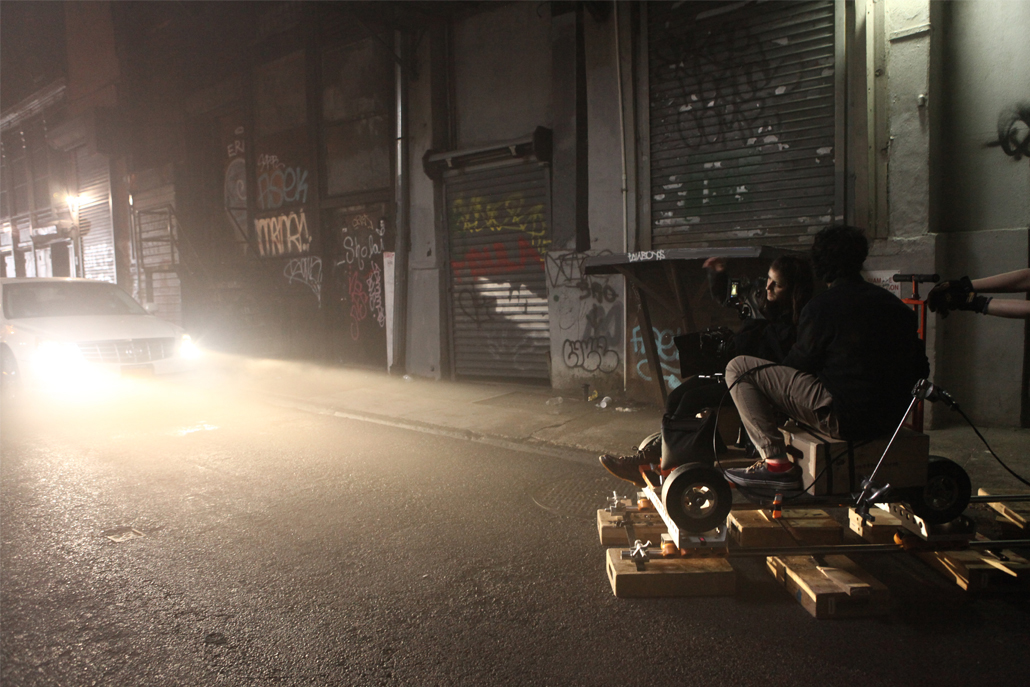 Two men in an alley filming a car with bright headlights at night