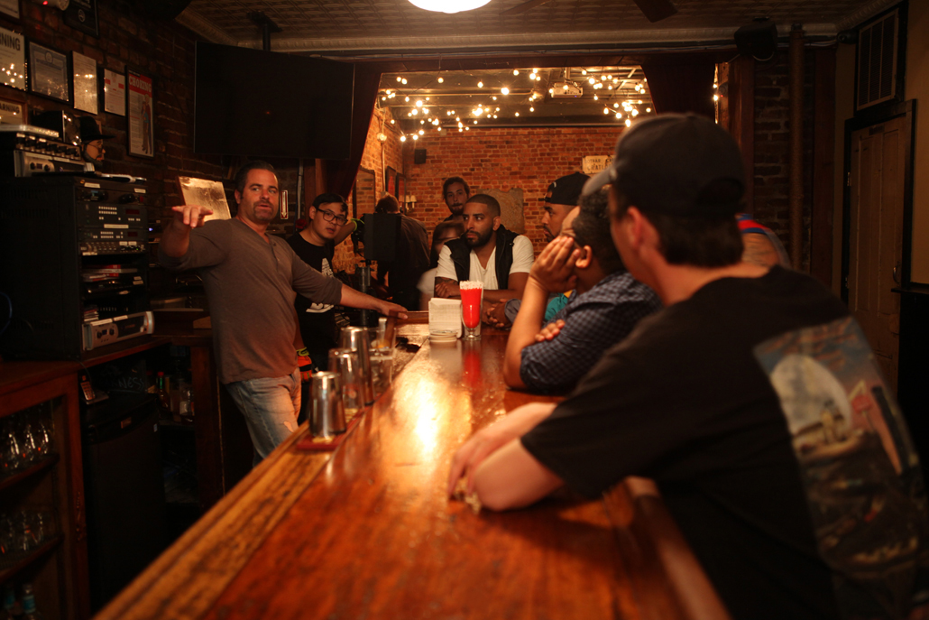 Men sitting at a bar listening to a bartender talk