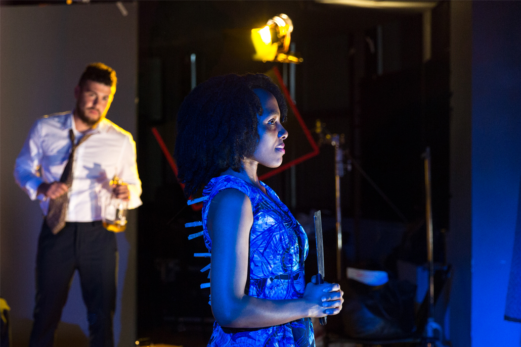 Woman on stage holding a knife with a man in the background