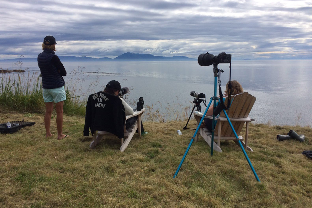 People sitting in chairs looking out at ocean with film equipment