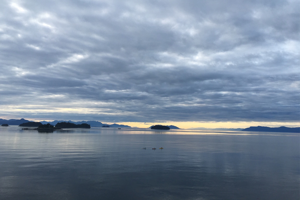 Ocean sunset with people canoeing and mountains in background