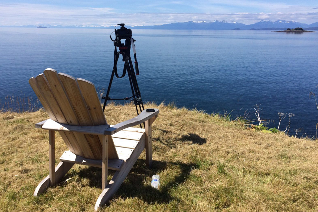 Wooden lounge chair with camera facing ocean and mountains