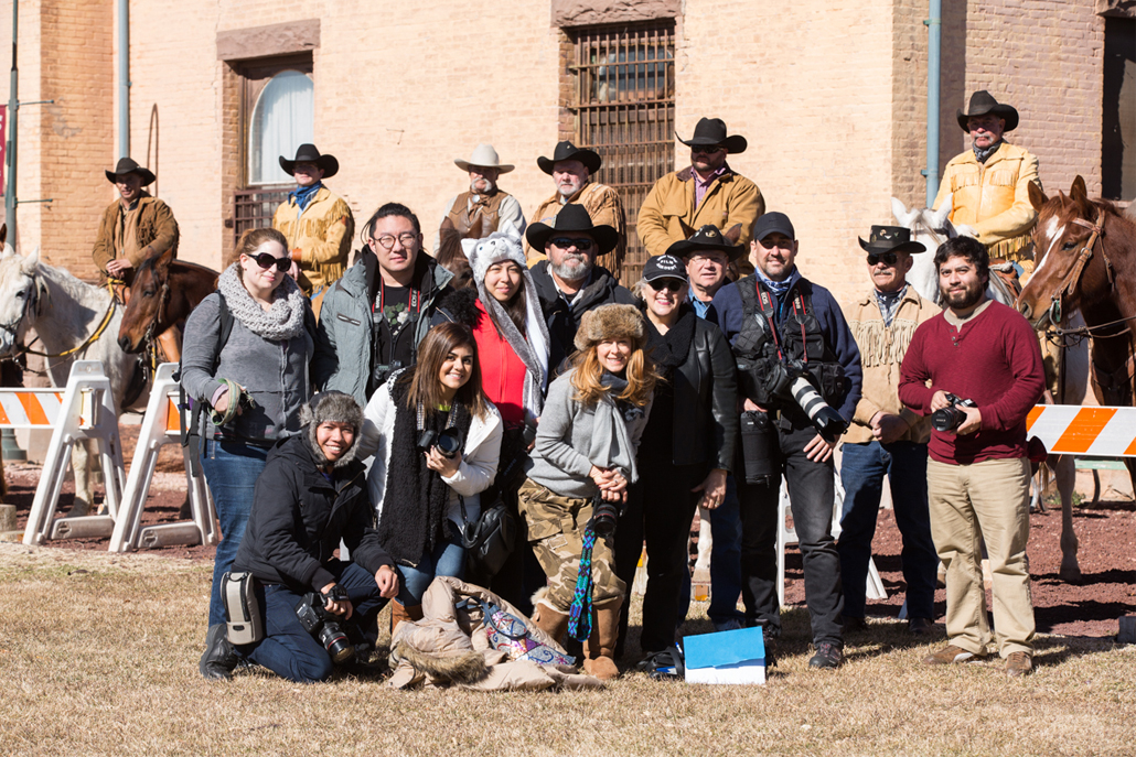 Group of people with camera equipment smiling in front of men on horses 
