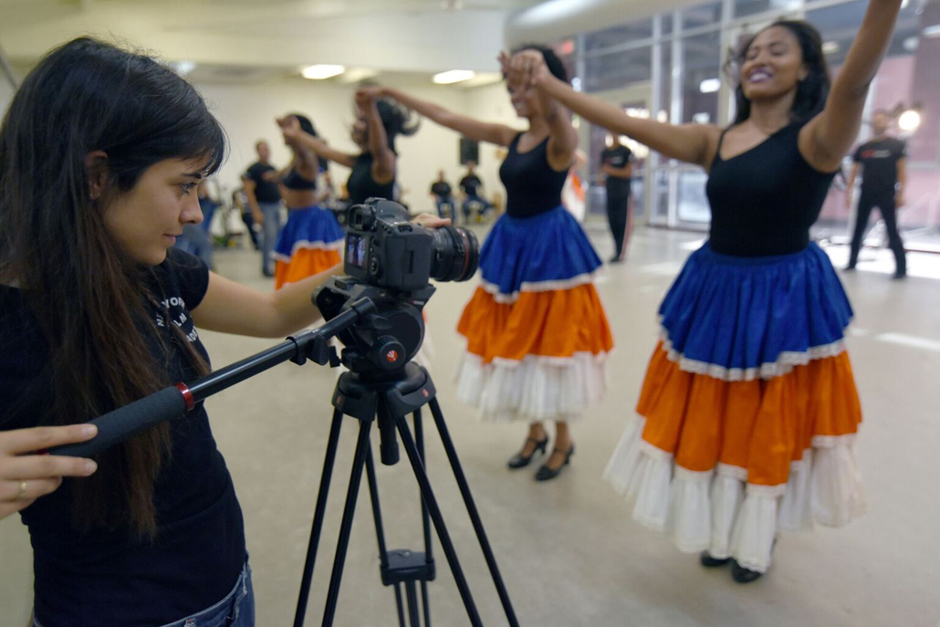 Woman videotaping women dancing in blue and orange skirts