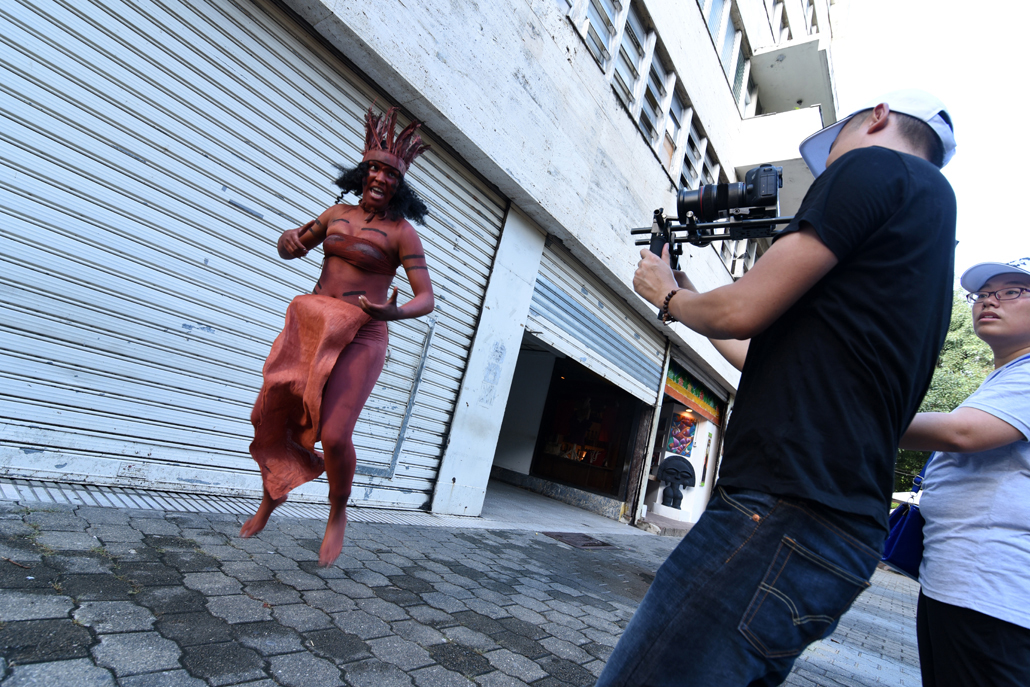 Man filming a woman in tribal clothing and body paint on the street