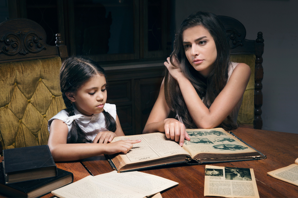 ﻿Mother and daughter sitting at table looking at old newpaper clippings and pictures