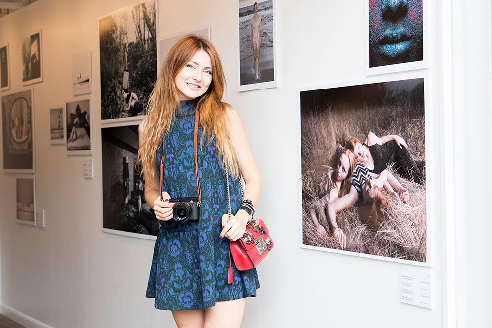 Woman posing with camera in front of photo exhibit