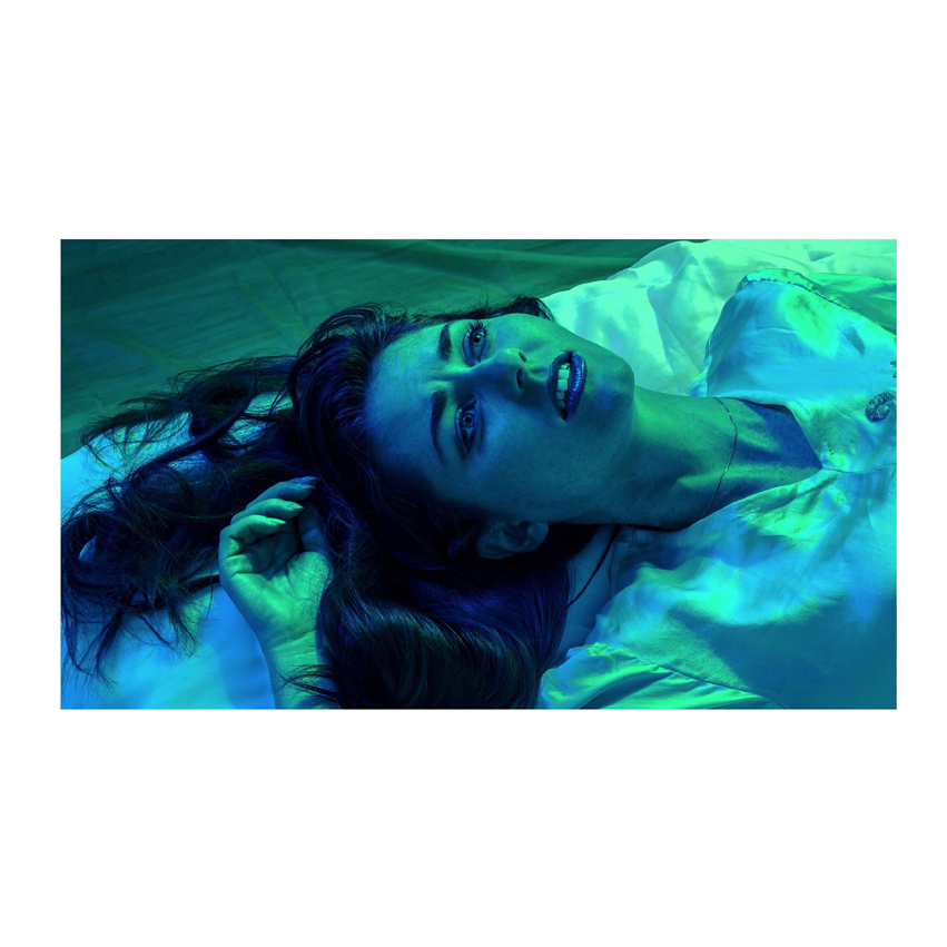 Woman laying on bed with eyes open and blue light shining on her