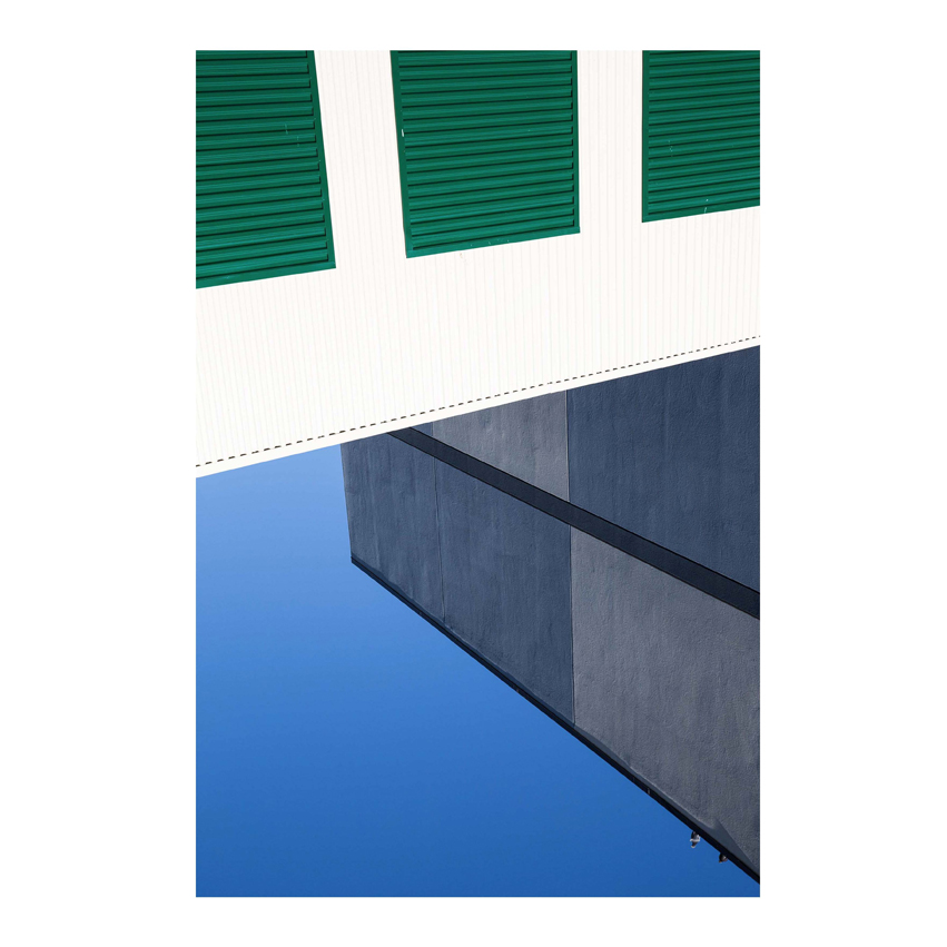 White wall with green shutters and photo of building and sky below it