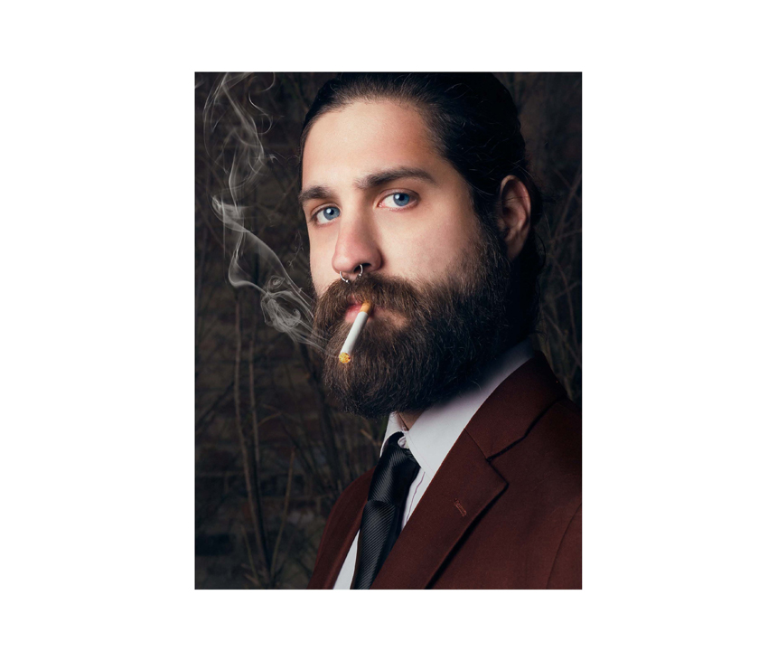 Man posing with beard and long hair smoking a cigarette in a suit