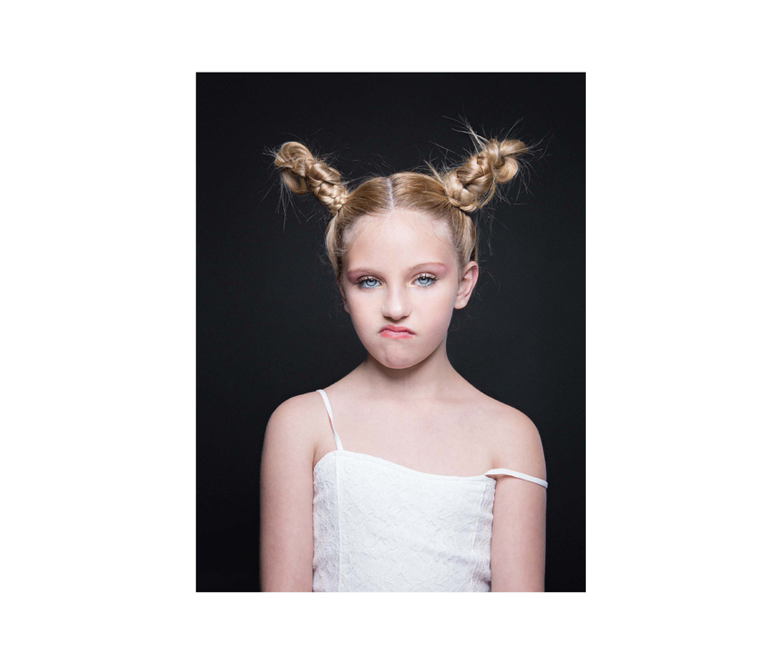 Girl with hair in buns frowning at camera