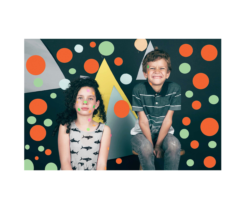 Two kids posing in front of polka dot wall with polka dots on bodies