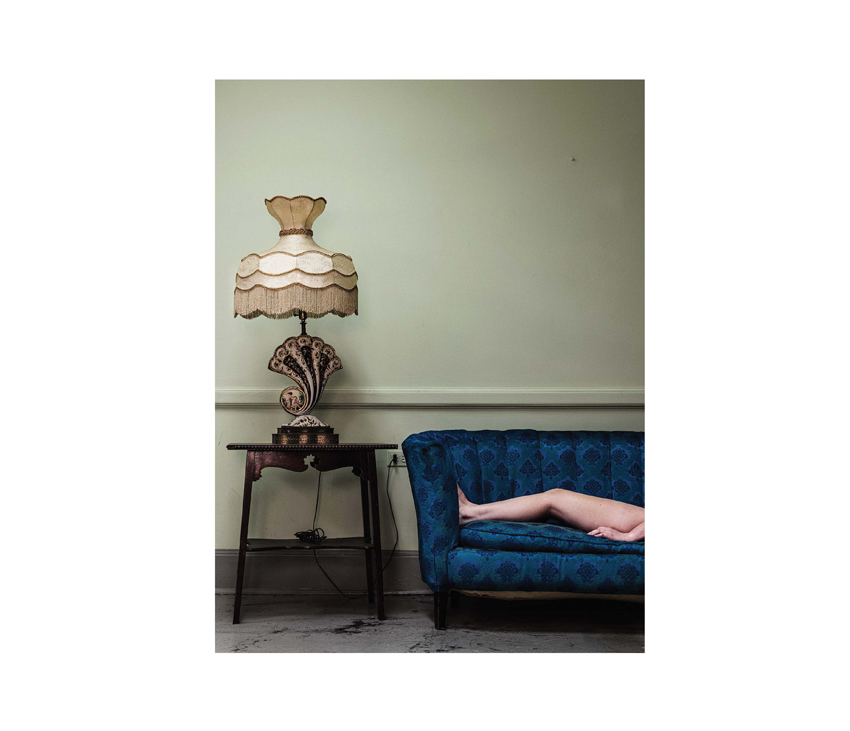 Naked legs laying on blue couch next to shell-shaped lamp