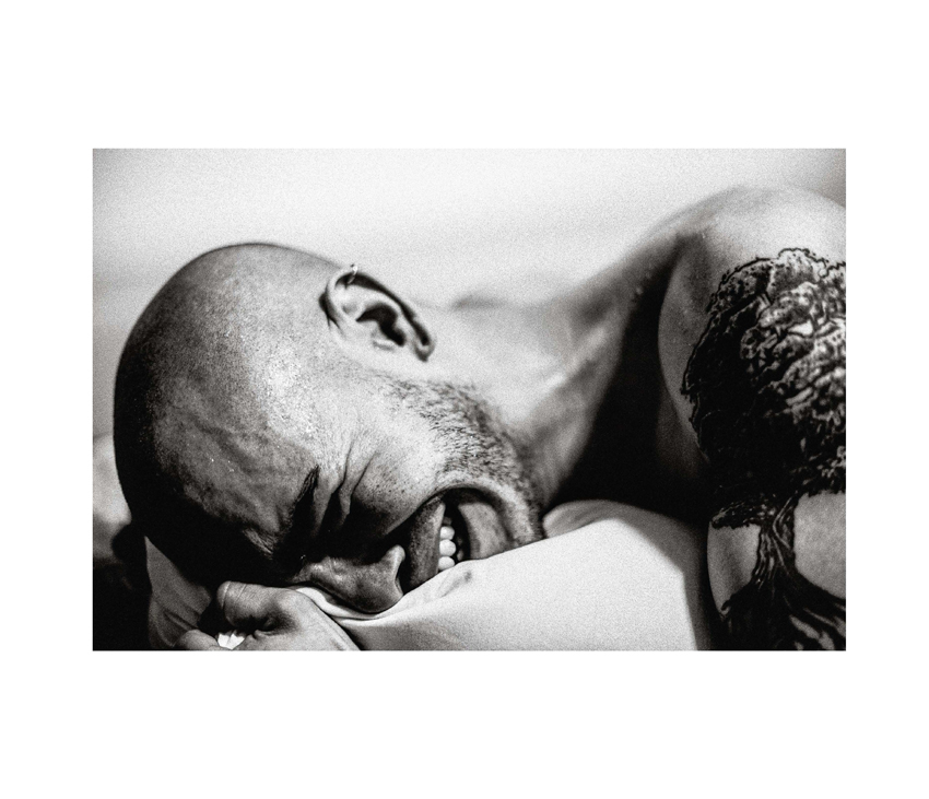 Man with tattoos crying and embracing pillow on bed