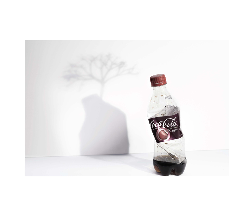 Crushed Coca-Cola Cherry bottle with shadow showing tree growing out of it