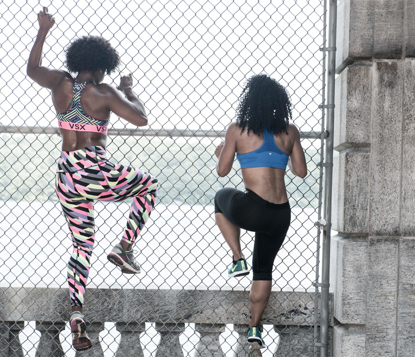 Two women stretching in workout clothes in front of stone wall