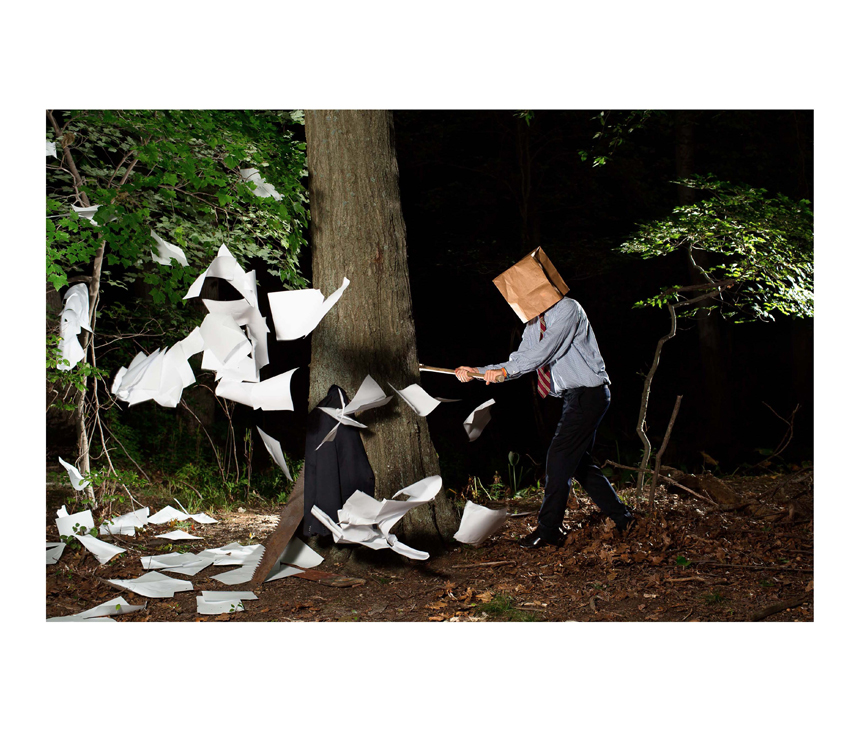 Man with paper bag over head chops down tree with papers flying around