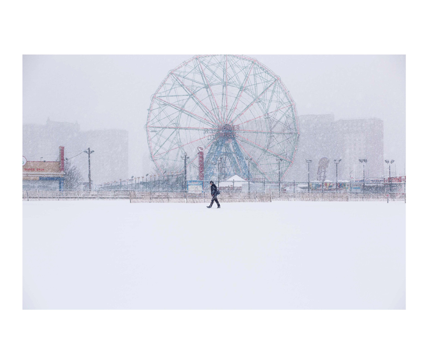 Man walking in snow in front of ferris wheel