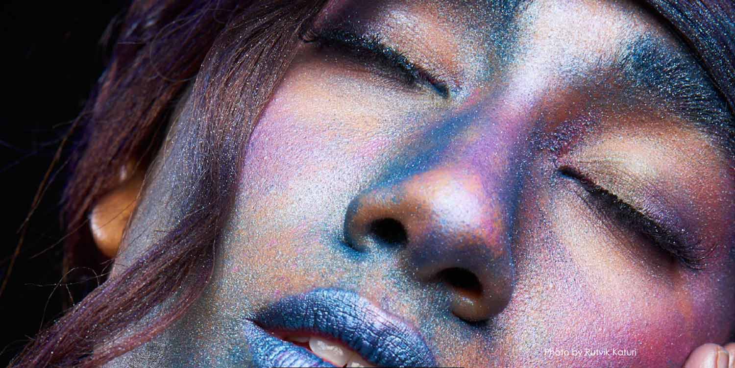 ﻿Upclose face of model covered with blue and purple glitter