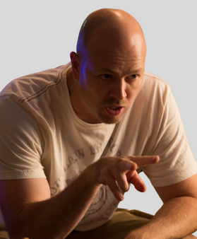 Man in a white t-shirt sitting and pointing while he explains something